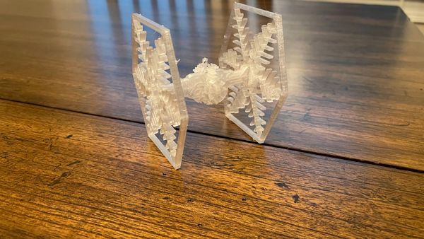 3D-Printed Clear Colored TIE Fighter Ornament on a wooden table